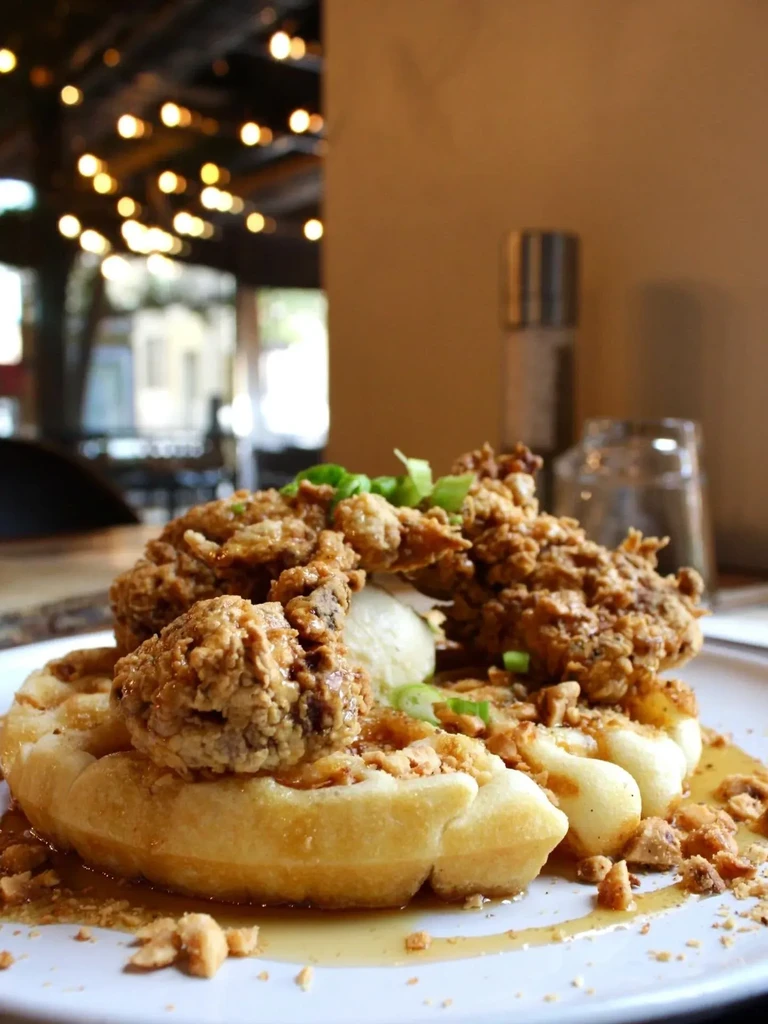 Crispy fried chicken and waffles with green onions, nuts, and syrup.