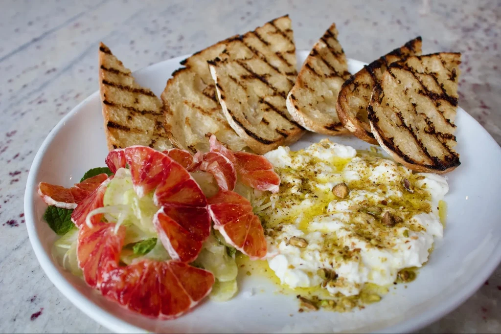 Gourmet dish with blood orange salad, burrata, pistachios, and grilled bread.