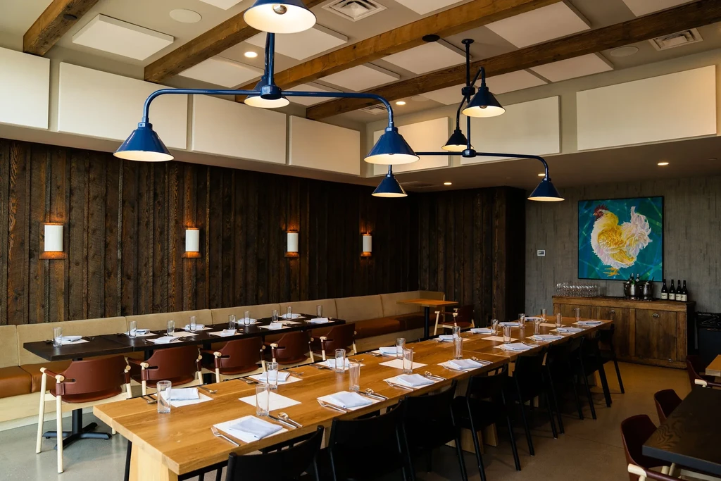 Modern-rustic restaurant dining room with wood walls, blue lights, and communal table.