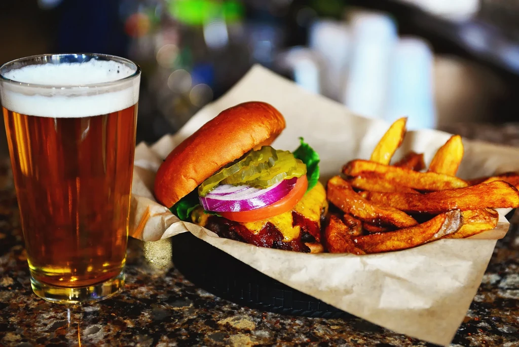 A cheeseburger, crispy fries, and a glass of beer on a counter.