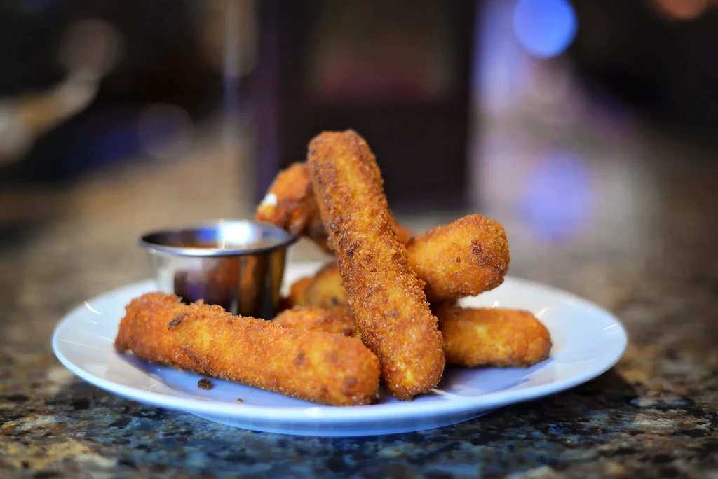 Golden-brown fried sticks and dipping sauce on a stone counter.