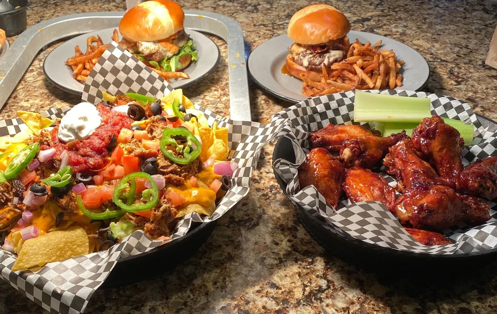 A spread of nachos, chicken wings, and two burgers with fries.
