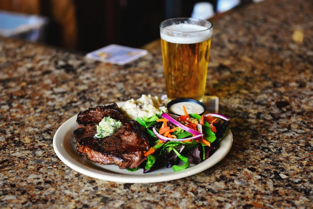 Grilled steak with herb butter, mashed potatoes, salad, and golden beer.