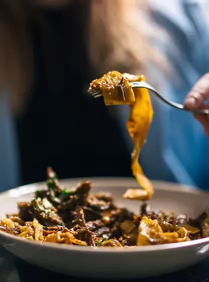 Close-up of a fork lifting saucy golden-brown pasta from a bowl.