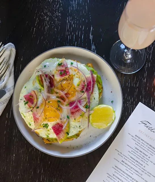 Overhead view of avocado toast with fried eggs, radish, and a pink drink.
