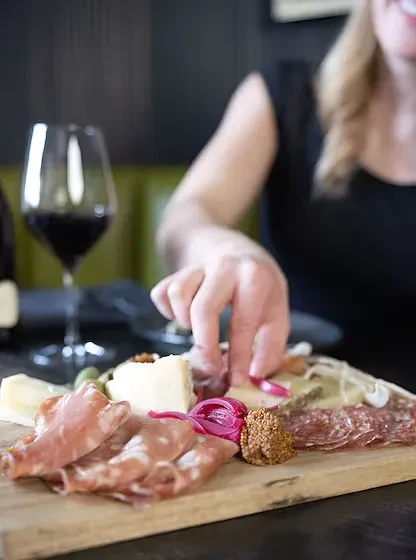 Hand reaching for appetizers on a wooden charcuterie board.