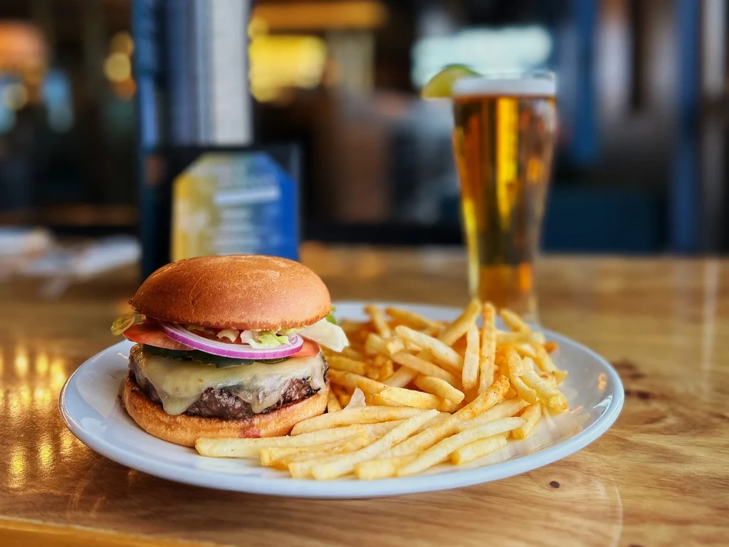 Cheeseburger, french fries, and beer on a wooden table.