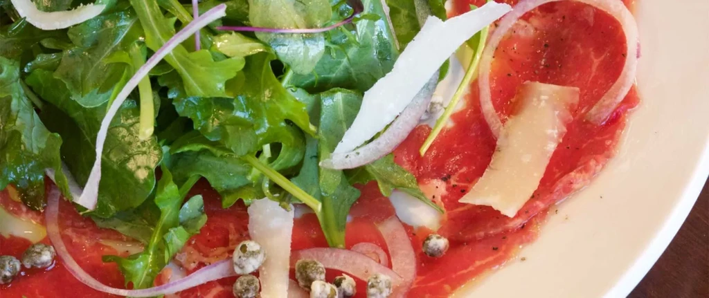 Thinly sliced meat carpaccio topped with arugula, Parmesan, red onion, and capers.
