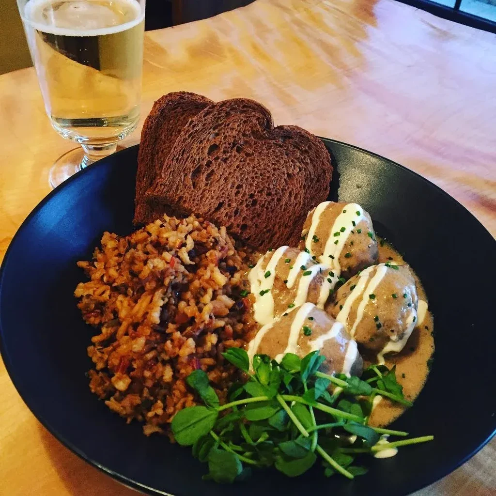 Five sauced meatballs, pilaf, heart-shaped bread, and drink in black bowl.