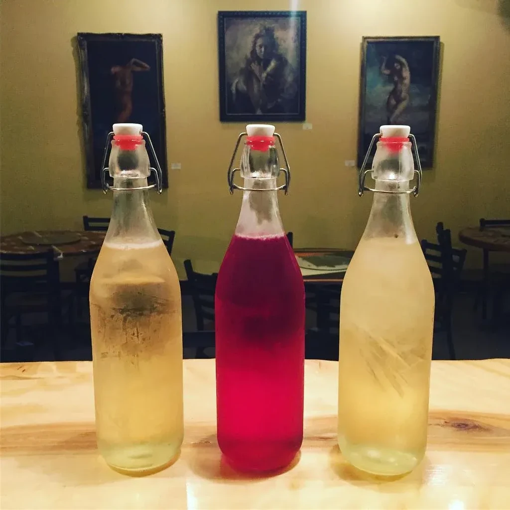 Three swing-top bottles: two yellow, one pink, on a wooden table.