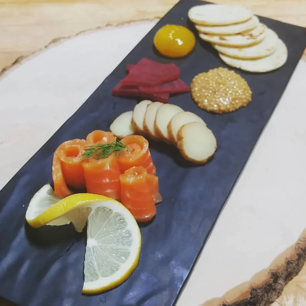 Black slate platter of smoked salmon rolls, lemon, beets, and crackers.