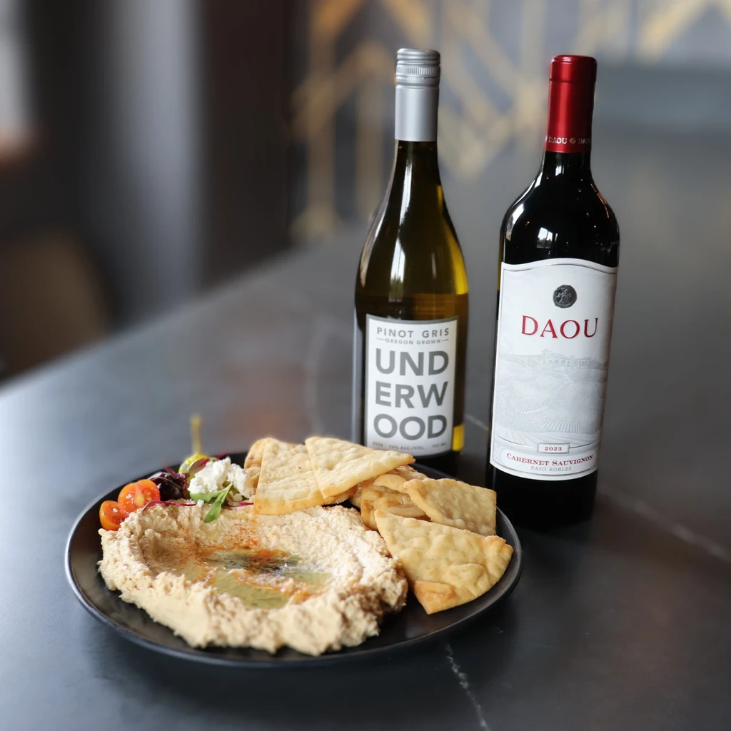 Hummus plate with pita, olives, feta, and two wine bottles.