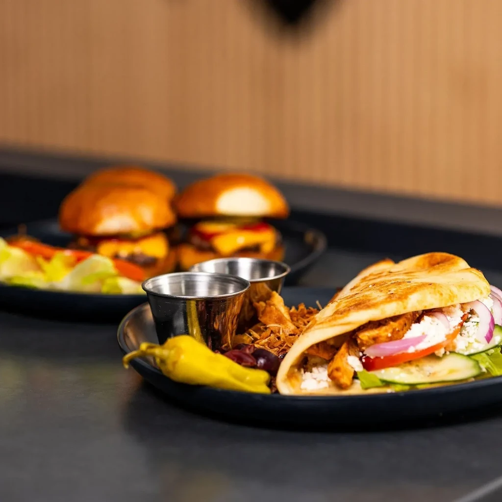 A chicken gyro, mini burgers, and salad on black plates.