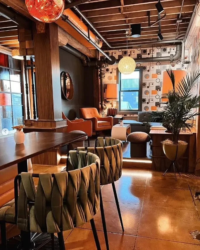 Eclectic restaurant lounge featuring olive chairs, orange seating, industrial ceiling.