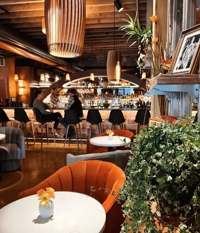 Stylish restaurant interior showing armchairs, a well-lit bar, and modern lighting.