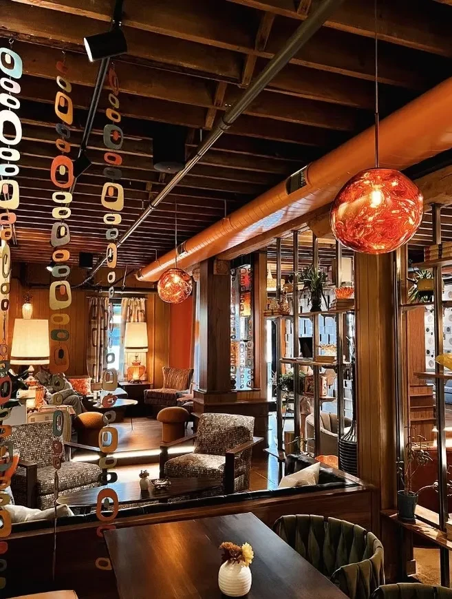 Vibrant, retro lounge with orange lighting, wood beams, and green chairs.