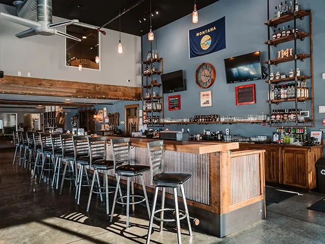 Empty industrial bar with long wooden counter, stools, and decor.