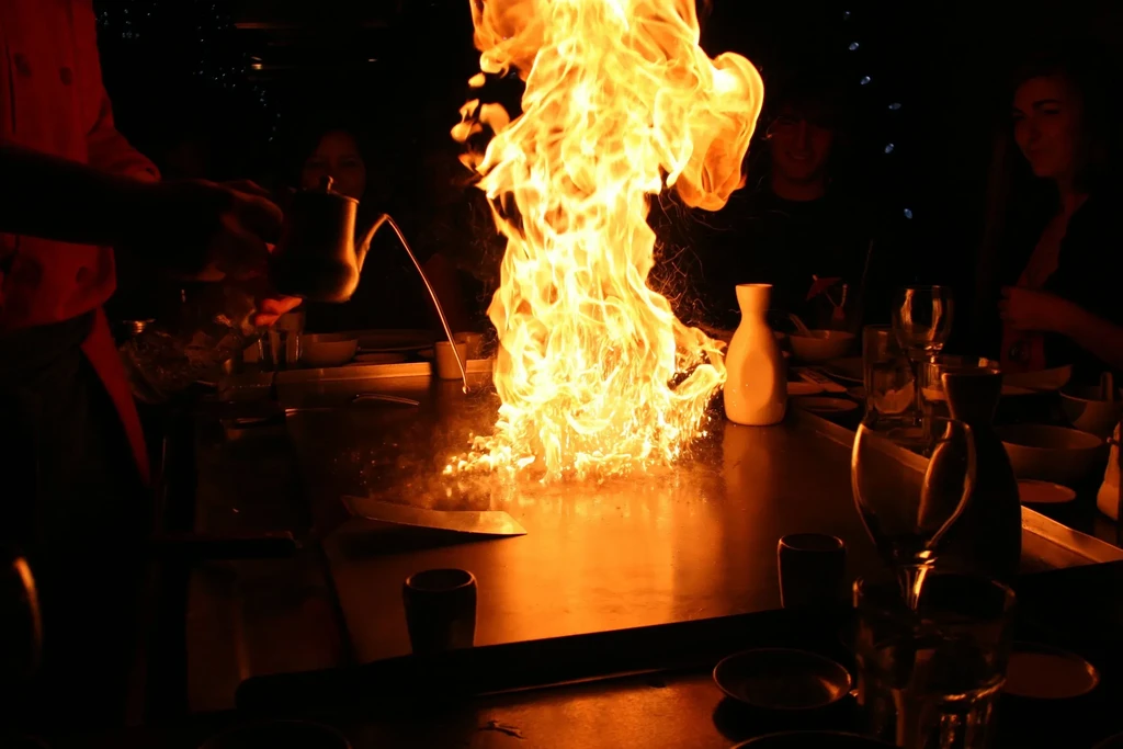 Dramatic fire erupts from a hibachi grill during a cooking show.