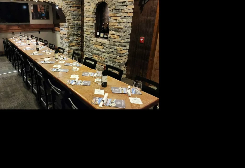 Dimly lit rustic dining room with long set table, stone walls.