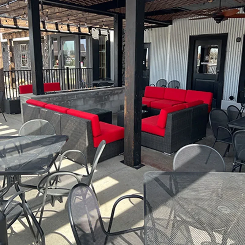 Outdoor patio with black wicker lounge seating, red cushions, metal tables.