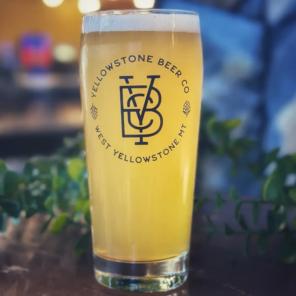 Tall glass of golden beer with foam and Yellowstone Beer Co logo.