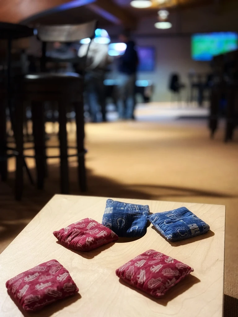Five cornhole beanbags: three red Indiana, two blue Colts, on wood.