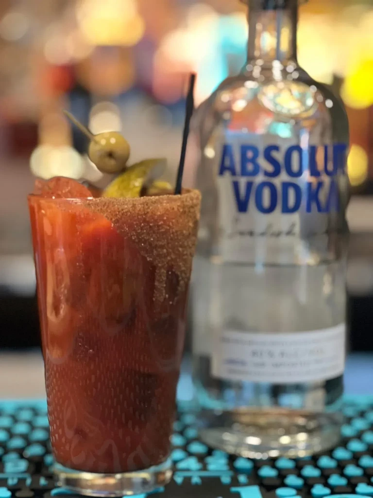 Garnished Bloody Mary on bar, Absolut Vodka bottle in background.