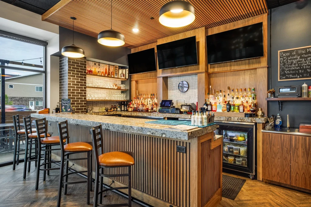 Modern restaurant bar with stone counter, liquor bottles, and TVs.