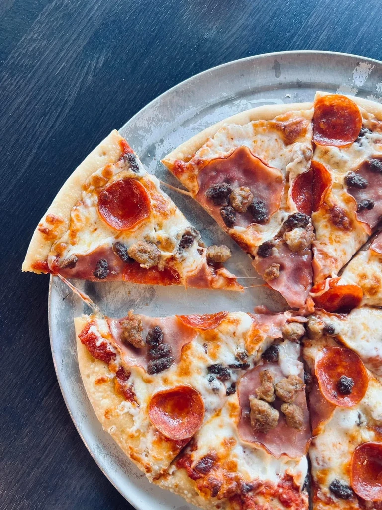 Overhead pizza with pepperoni, sausage, ham, and stretchy melted cheese.