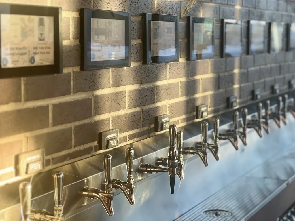 Polished chrome self-pour beverage taps on a rustic brick wall.