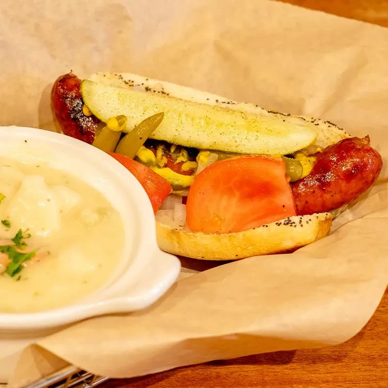 Grilled hot dog with mustard, relish, pickle, and creamy soup.
