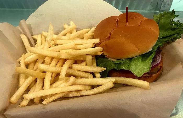 Classic hamburger with toothpick and golden french fries in a paper basket.