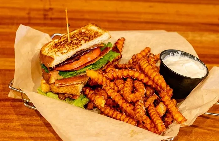 Grilled club sandwich, crinkle-cut fries, and dipping sauce in a metal basket.