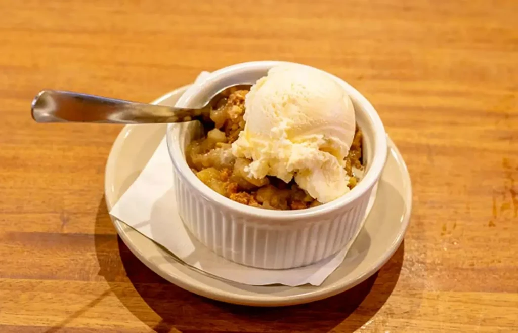 Apple crumble topped with vanilla ice cream in a ramekin, with a spoon.