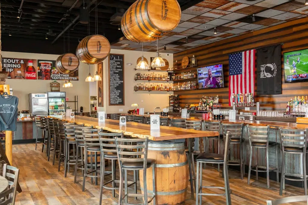 Rustic American-themed bar interior with whiskey barrel decor, flags, and TVs.