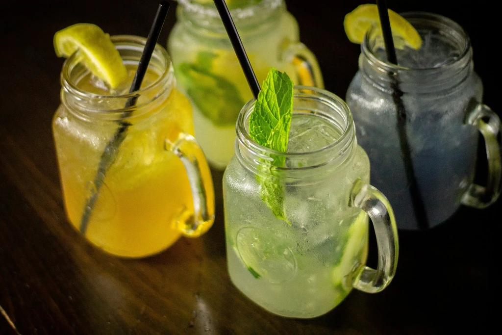 Close-up of four colorful drinks in mason jars with garnishes.