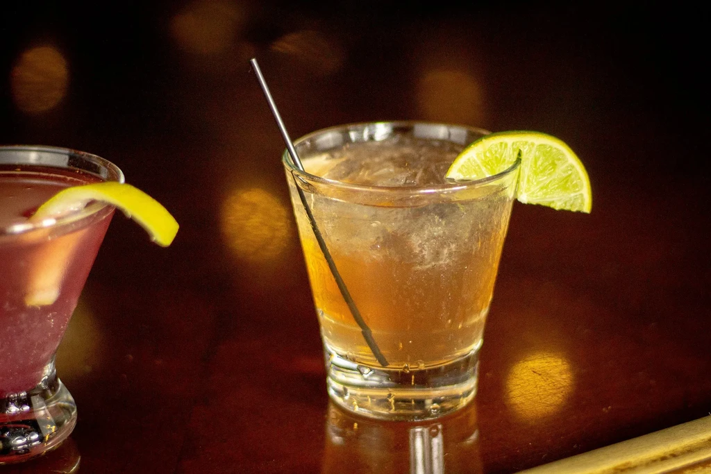 Two colorful cocktails with lime and lemon garnishes on a dark surface.