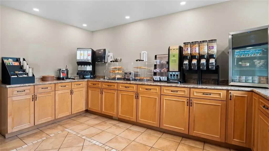 Hotel self-service breakfast counter with coffee, juice, pastries, and cereal.