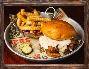 Burger with creamy sauce, bacon, fries, pickles in a metal tray.