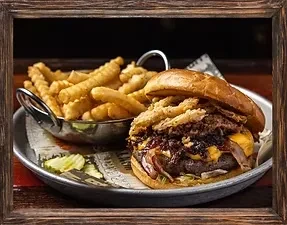 Gourmet burger, crinkle-cut fries, and pickles on a deli-lined metal tray.