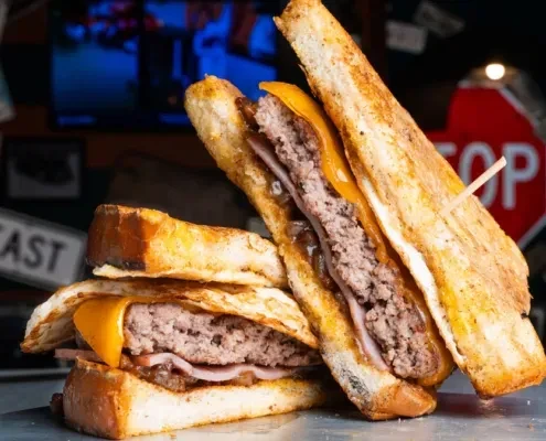 Stacked burger with two meat patties, melted cheese, ham, and onions.