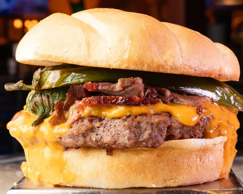 Close-up beef burger with melted cheese, crispy bacon, and roasted chiles.