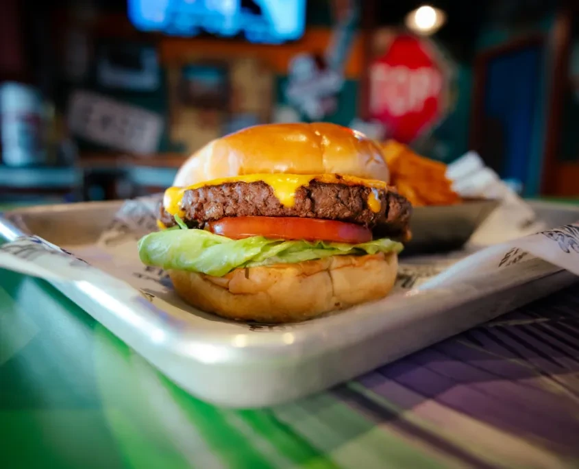 Close-up cheeseburger with fries on a tray in a blurred restaurant.