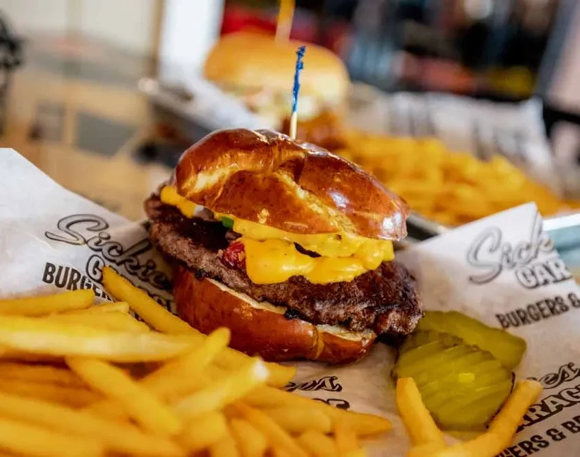 Close-up cheeseburger on a pretzel bun, served with fries and pickles.