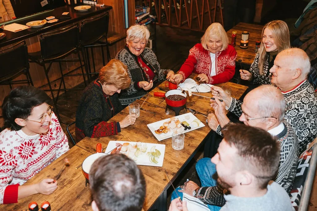 Friends laughingly share fondue, dipping bread and fruit at a cozy bar.