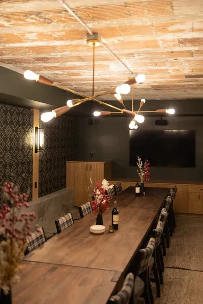 Rustic private dining room with long table, plaid chairs, Sputnik lights, accent wall.