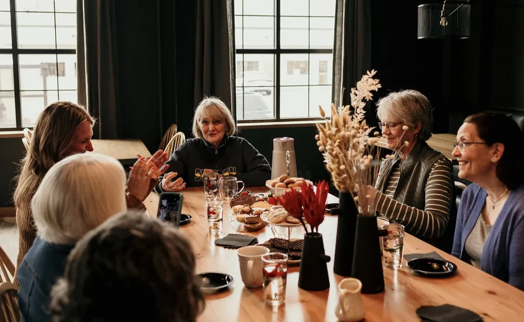 Older women laughing and conversing at a cafe table with desserts.