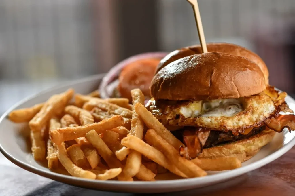 Close-up of a burger with egg, bacon, cheese, and crispy fries.