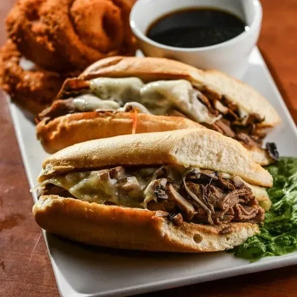 Two cheesy meat sandwiches, onion rings, and dipping sauce on a plate.