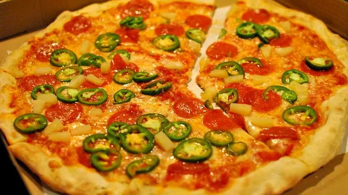 Whole pizza with jalapeños, pepperoni, pineapple, one slice separated.